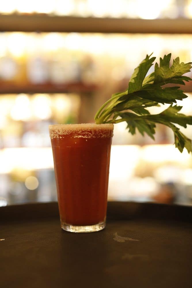 Drink vermelho com folhas de salsão no balcão do Janelas